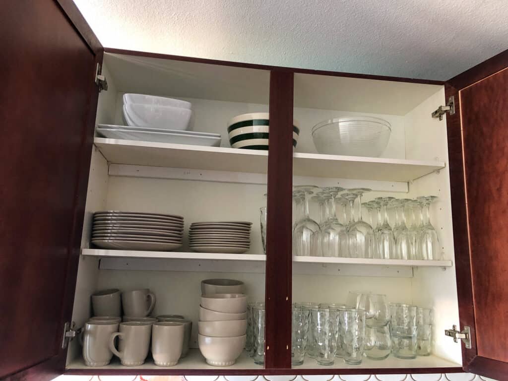 The kitchen cabinet is fully stocked with plates, bowls, glasses, and serving dishes